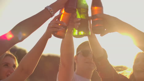Young-people-raise-their-hands-up-and-clink-glasses-of-beer-in-bright-glass-bottles-on-the-open-air-summer-party.